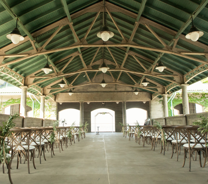 Outdoor wedding venue with rows of empty chairs and green ceiling.